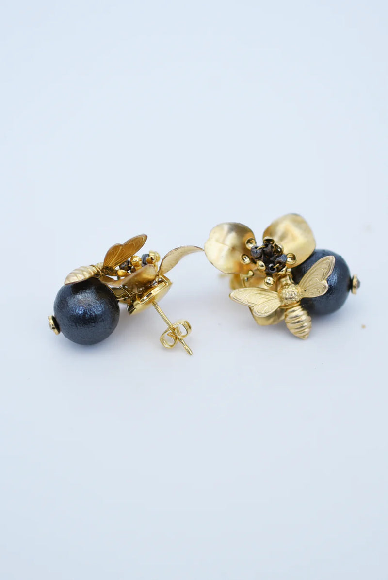 Brass bee and begonia blossom earrings on a texutred linen surface with a blurred background