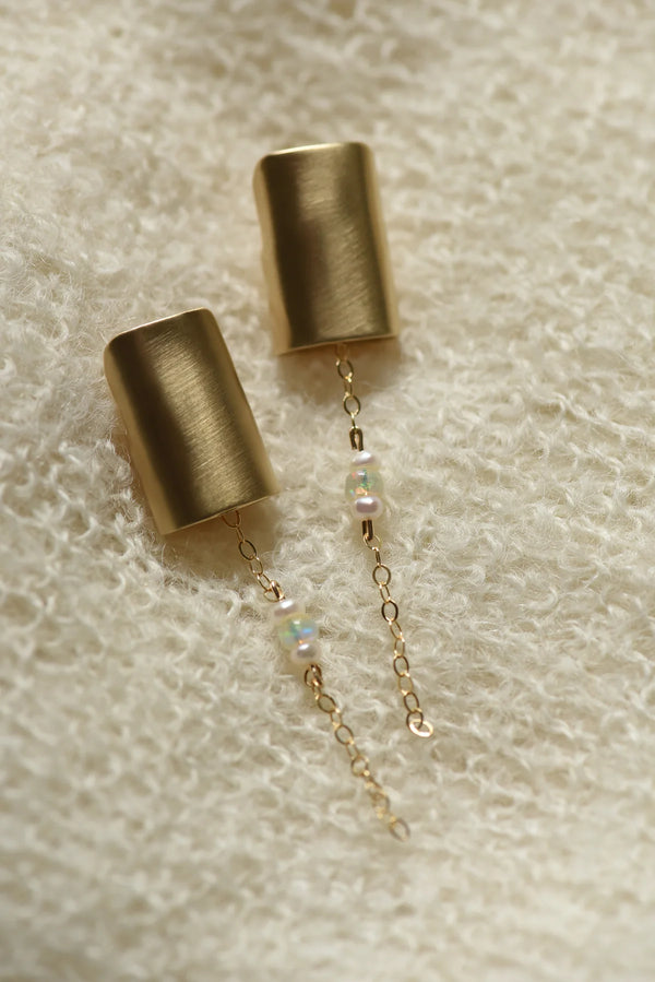 Close-up of a brass earring with a chain and opal and pearl beads