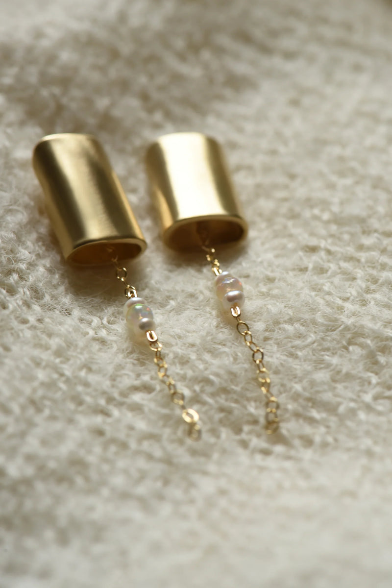 Close-up of a brass earring with a chain and opal and pearl beads