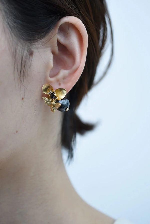 Close-up of an ear wearing a Brass bee and begonia blossom earrings with white background