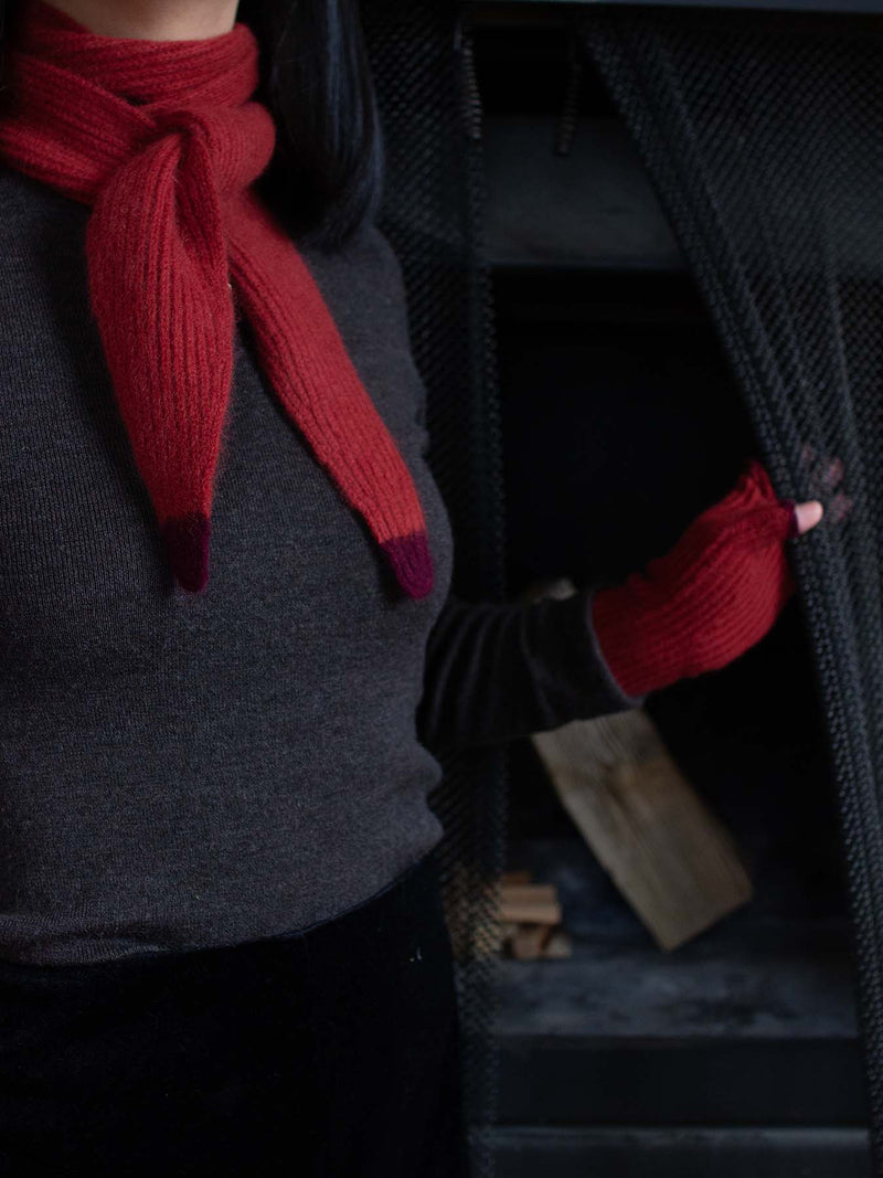 Person wearing a red knitted scarf red knit gloves in a dark setting