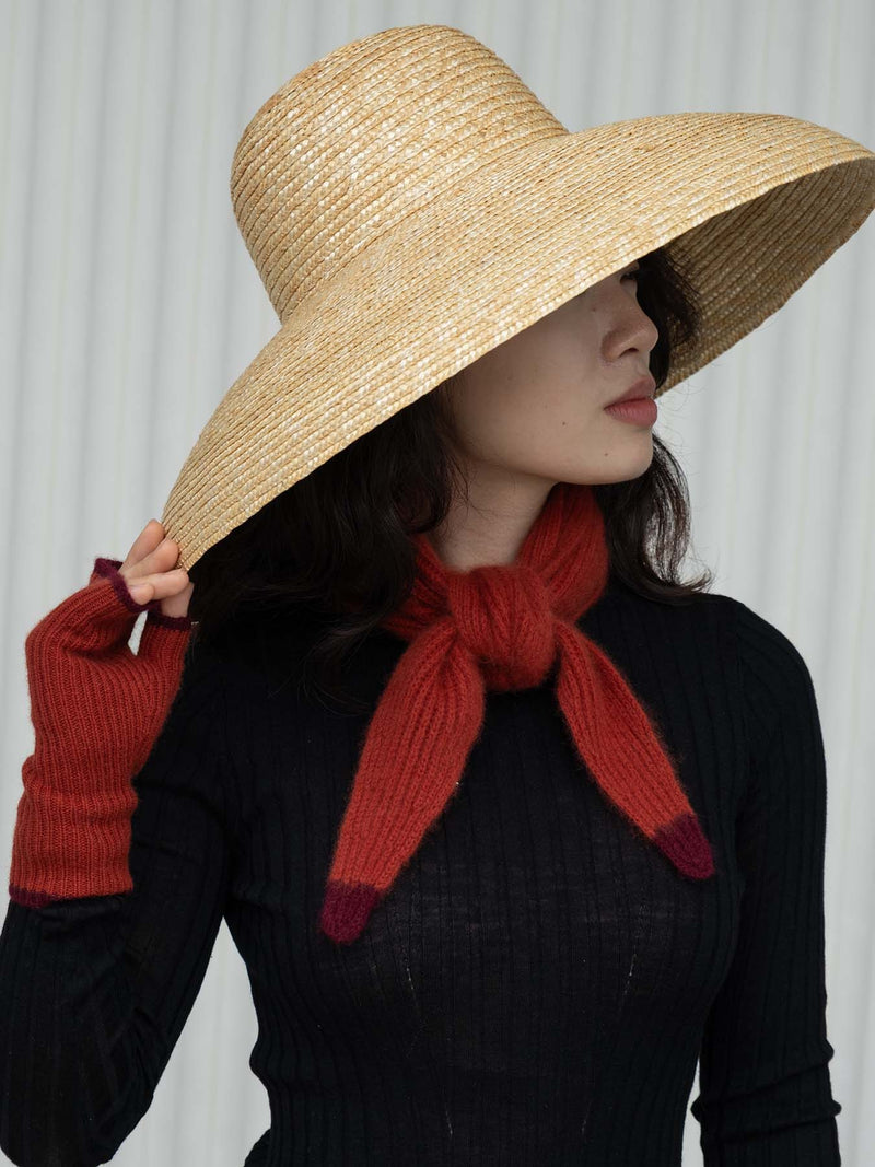 Person wearing a wide-brimmed straw hat and knit red scarf against a white background