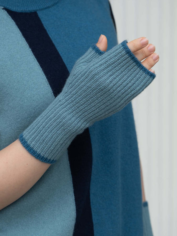 Blue knitted fingerless gloves worn by a person against a white background