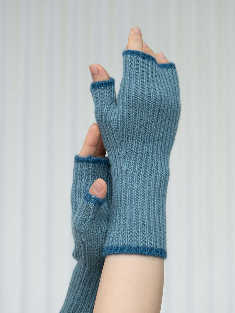 Blue knitted fingerless gloves held by a hand against a white background