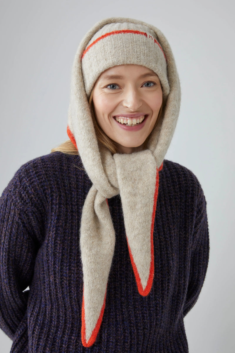 Person wearing a beige scarf with orange trim on a plain background