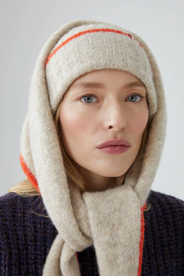 Person wearing a beige knitted hat and scarf with orange trim on a plain background