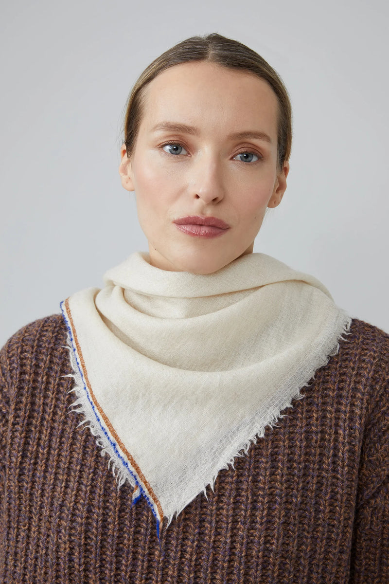 Woman wearing a beige scarf with blue and brown stripped trimming against a plain background