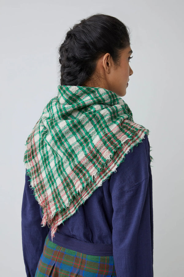 Person wearing a green, red and white gingham scarf on a plain background