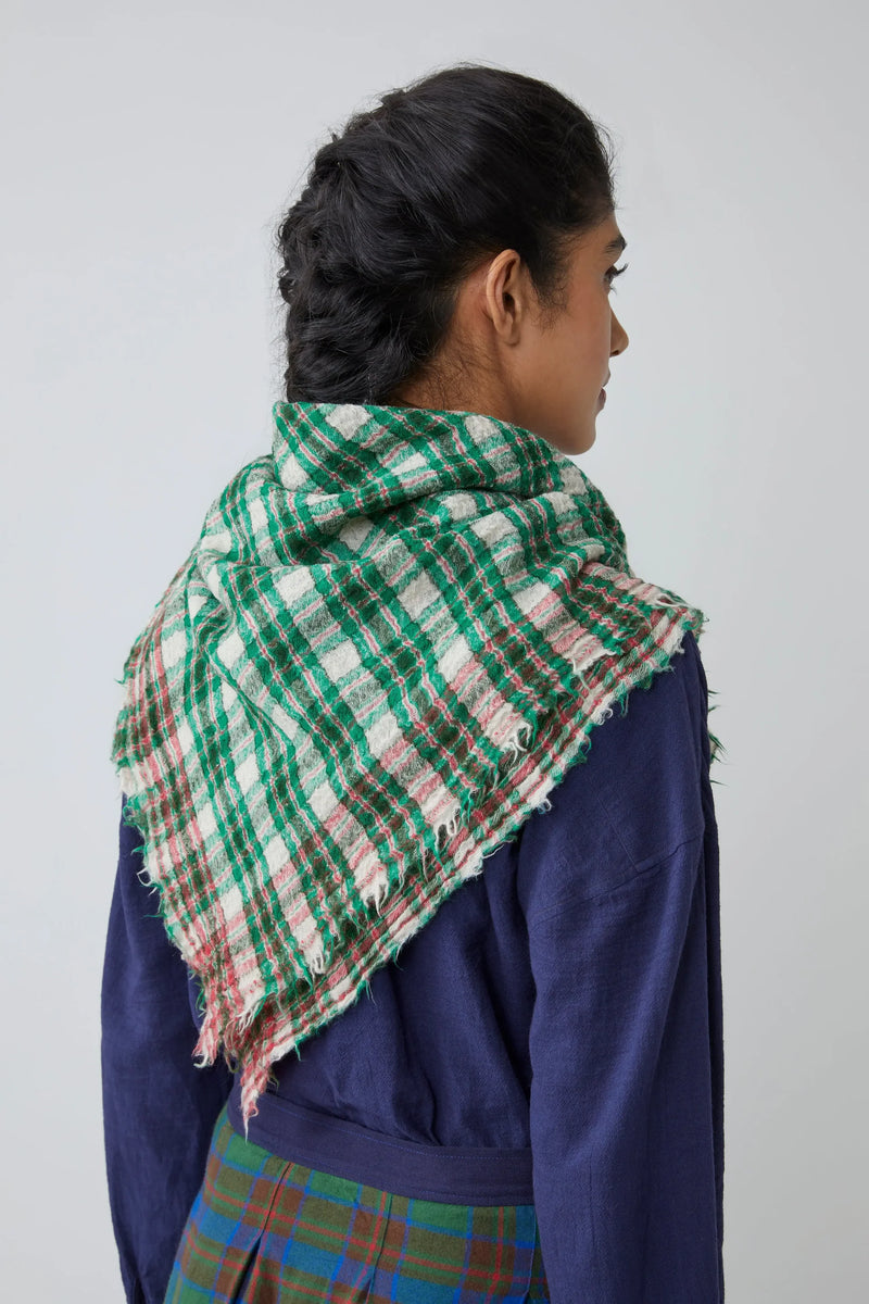 Person wearing a green, red and white gingham scarf on a plain background