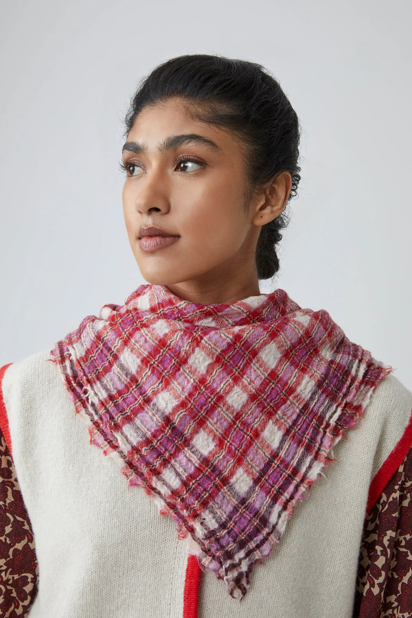 Woman wearing a pink, red and white gingham scarf over a patterned top against a plain background