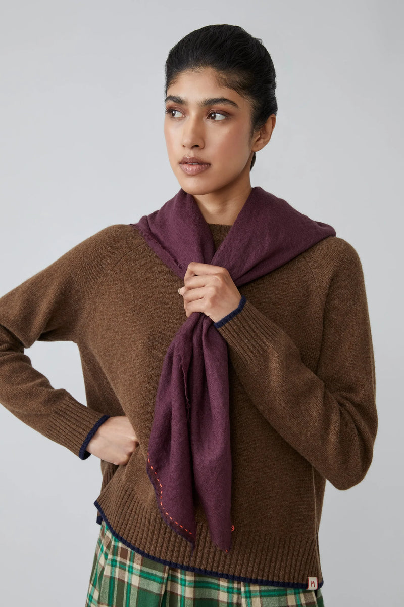 Woman wearing a brown sweater and purple scarf against a plain background