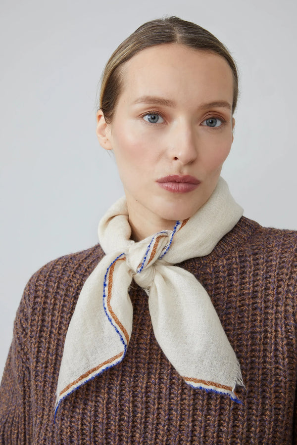 Woman wearing a beige scarf with blue and orange stripes against a light gray background