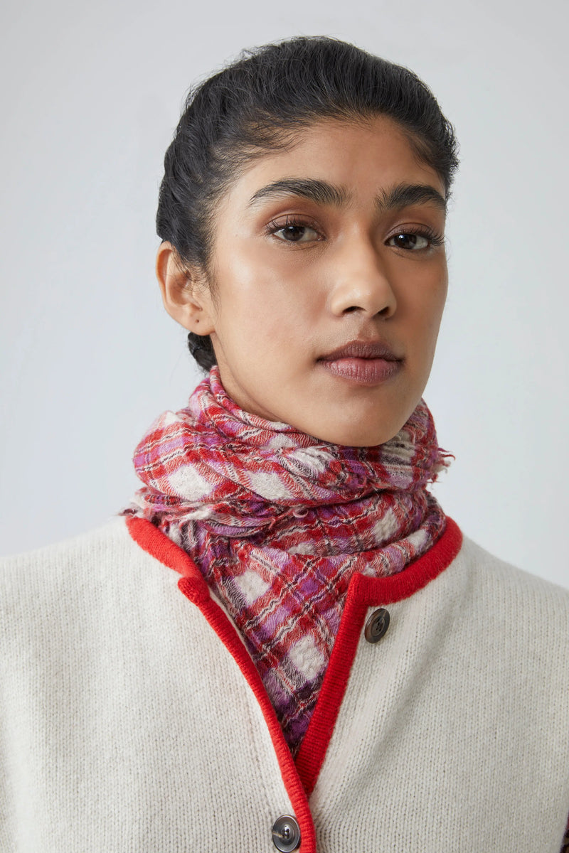 Woman wearing a pink, red and white gingham scarf on a plain background
