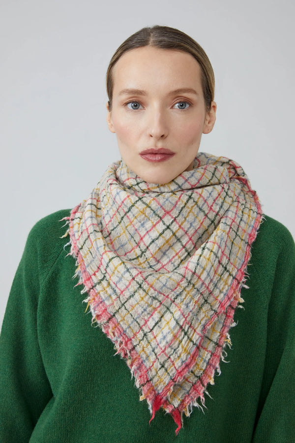Woman wearing a pink, green, yellow and blue gingham scarf and green sweater against a plain background