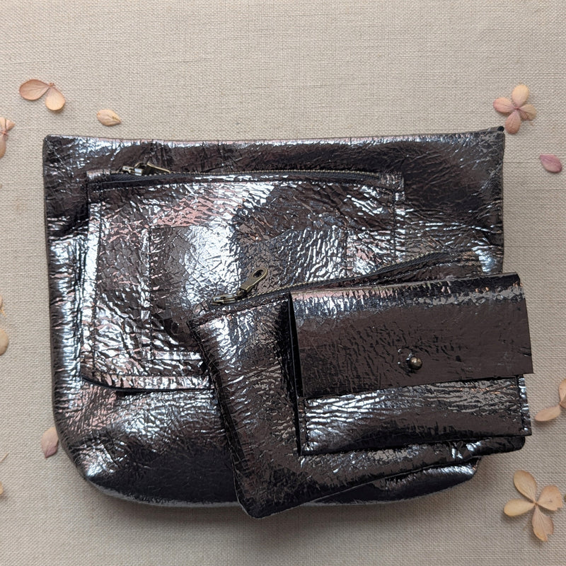 Shiny metallic clutch and wallet set on a beige background with scattered flowers.