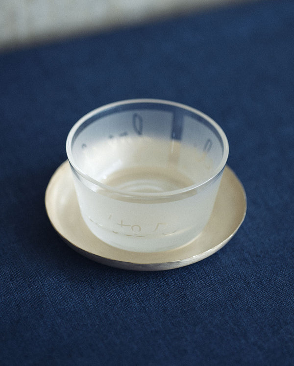 Clear glass cup on a small silver round tray.

Fog Linen round silver brass plate tray dish serving catch all home decor kitchen Boston gift shop store boutique