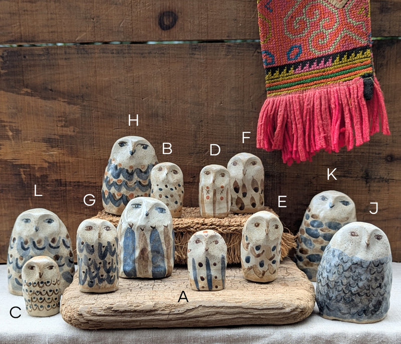 Collection of ceramic owl figurines on a wooden base with a colorful scarf in the background.