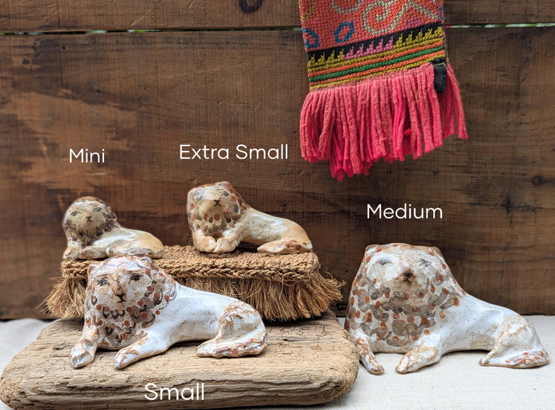 Four ceramic lion figurines of different sizes on a wooden surface with a colorful fabric hanging in the background.