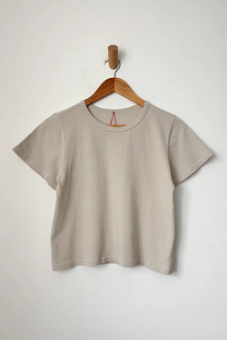 Beige little boy t-shirt from Le Bonne Shop on a wooden hanger against a white background