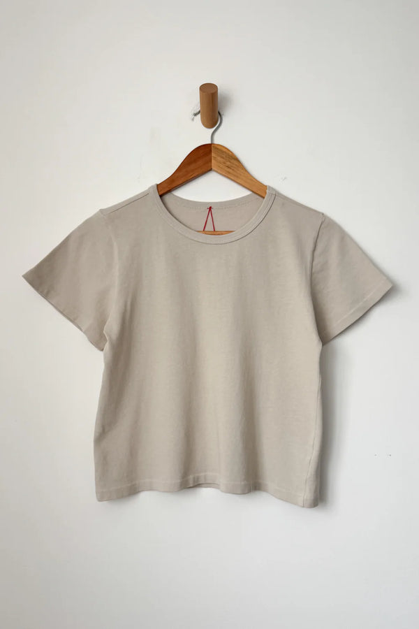 Beige little boy t-shirt from Le Bonne Shop on a wooden hanger against a white background