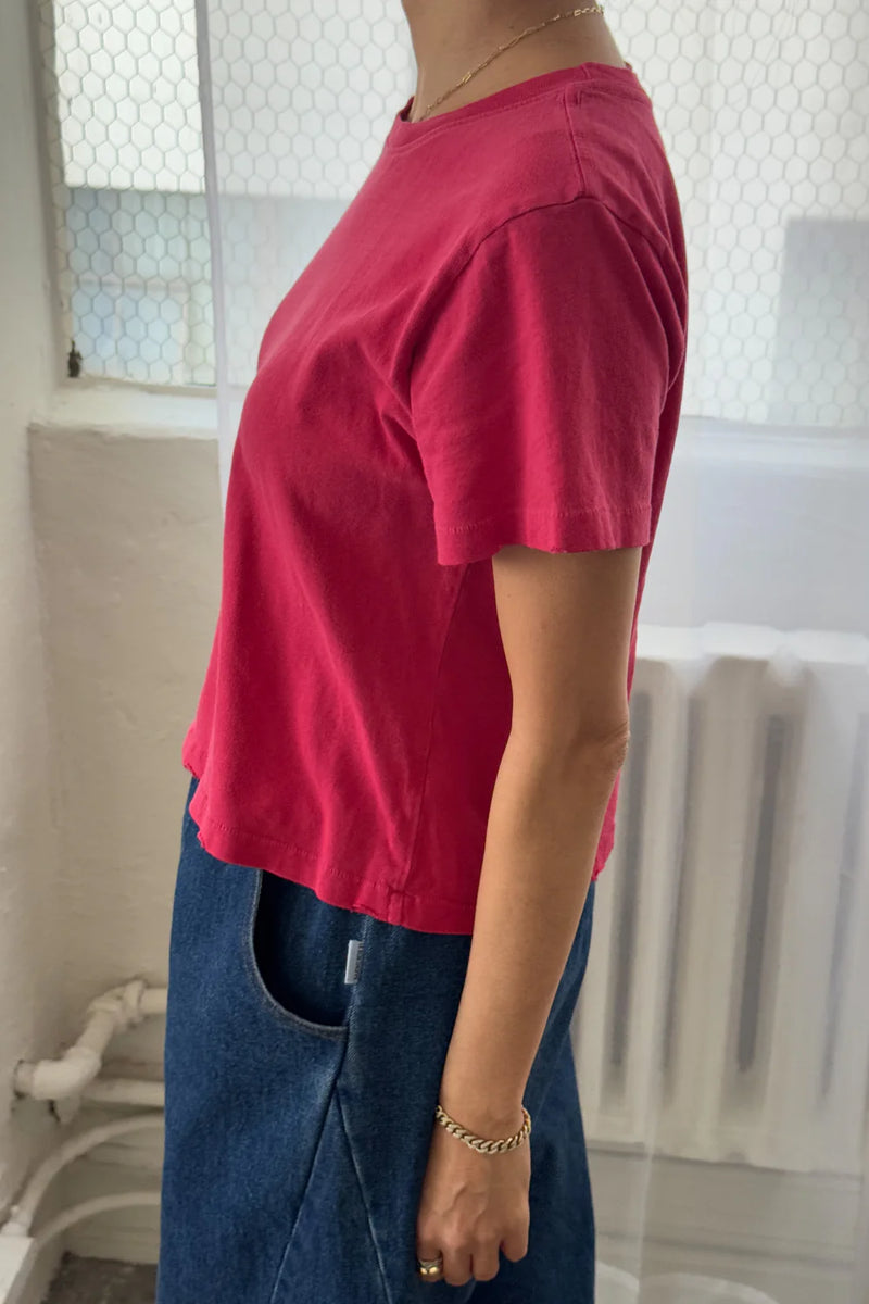 Person wearing a Le Bon Shoppe Darling T shirt in Red Pepper and blue jeans in a room with a radiator.
