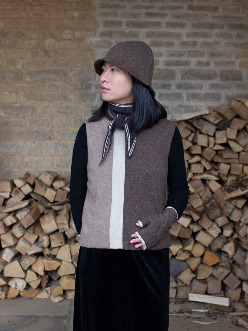 Person wearing a dark brown scarf with white stripes over a brown and beige outfit.