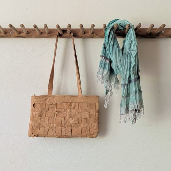 Brown woven bag and green scarf hanging on a wooden rack against a white wall.

Stitch and Tickle Woven Horizonal Shoulder Baguette Tote Bag one of a kind unique leather shop boston New England handmade sowa gift store 