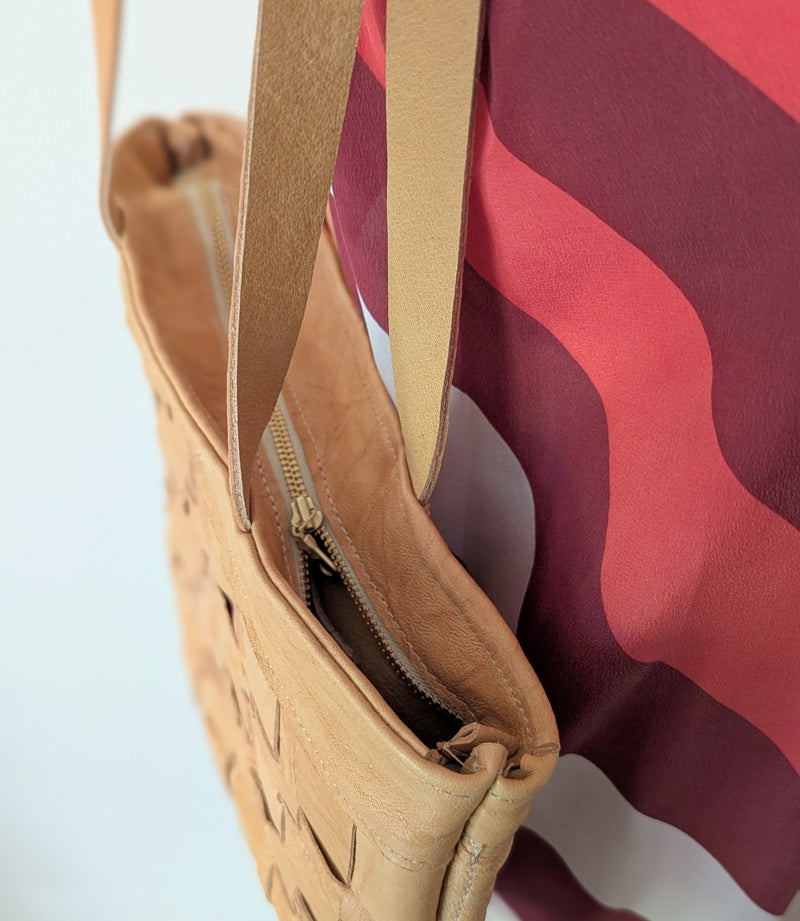 Close-up of a beige handbag with a red and purple patterned dress in the background. 

Stitch and Tickle Woven Horizonal Shoulder Baguette Tote Bag one of a kind unique leather shop boston New England handmade sowa gift store 