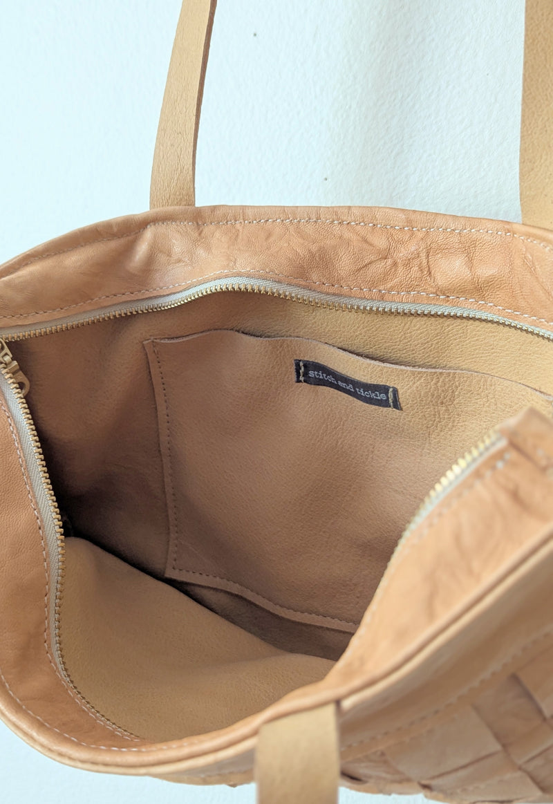 Inside of beige leather handbag with a Stitch and TIckle label on a white background. 

Stitch and Tickle Woven Horizonal Shoulder Baguette Tote Bag one of a kind unique leather shop boston New England handmade sowa gift store 