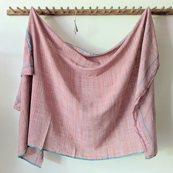 Fabric draped over a wooden rod against a white wall. Auntie Oti Indian cotton lungi woven Khadi wrap throw sarong beach blanket towel tablecloth shop Boston sowa boutique gift store handmade 