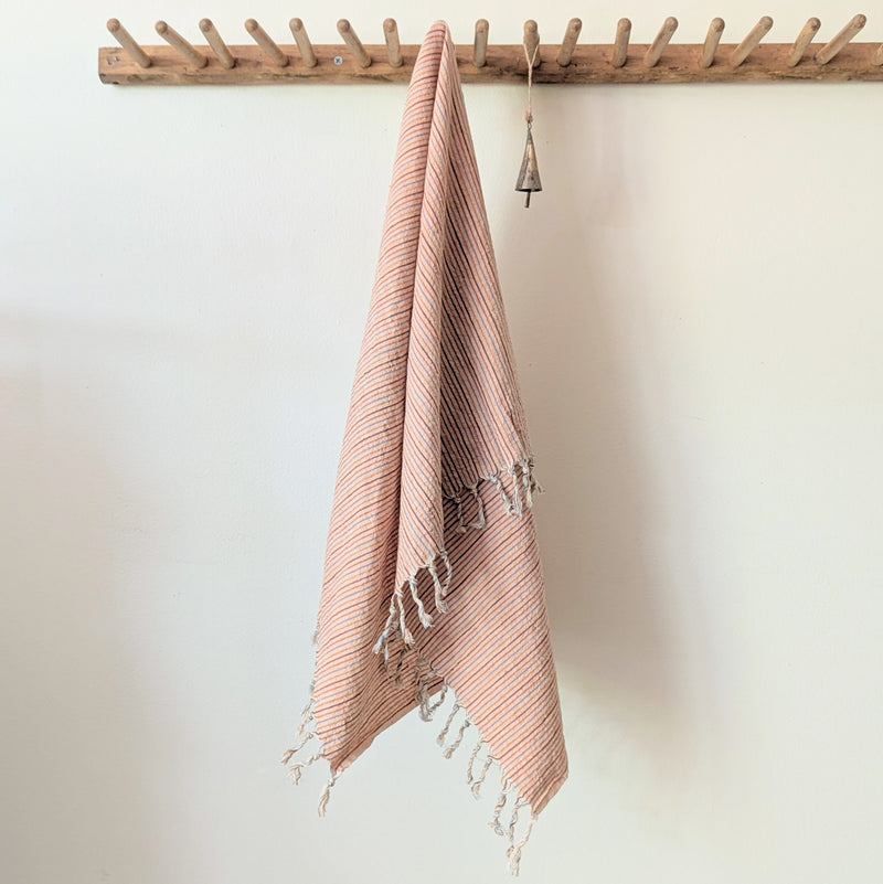 Pink towel with tassels hanging on a wooden rack against a white wall. Auntie Oti hand woven khadi cotton kitchen towel natural dye handmade shop Boston sowa gift store boutique