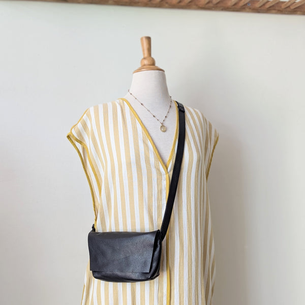 Mannequin wearing a yellow and white striped dress with a black crossbody bag against a plain background. Stitch and Tickle handmade leather mini messenger bag crossbody made in Boston made in usa leatherwork leathercraft SoWa shop boutique gift store