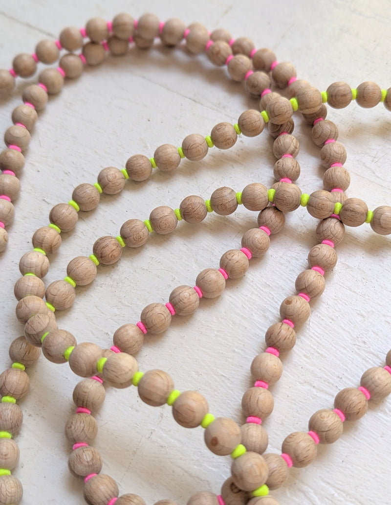 Wooden beaded phone necklace with pink and yellow accents on a light wooden surface. Ina Seifart Handikette Phone Necklace handmade wood beads gift shop sowa boston fashion accessories independent boutique lanyard keychain