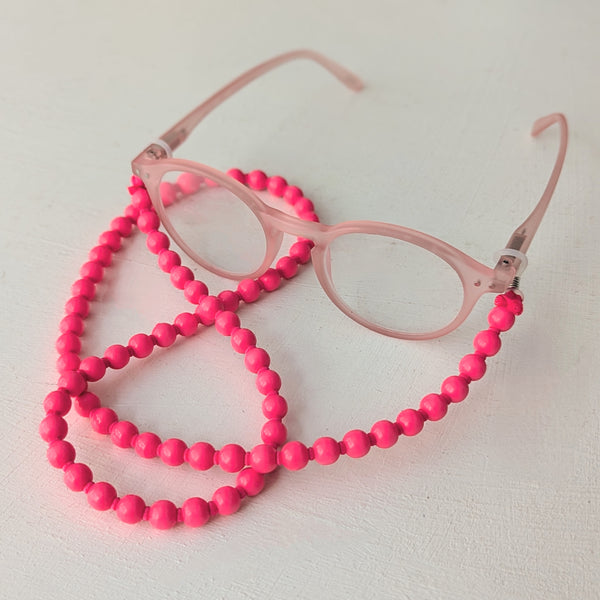 Pink beaded eyeglass holder with pink eyeglasses on a light background. Ina Seifart  Brillenkette Eyeglasses Chain necklace beads wood handmade gift shop sowa boston fashion accessories independent boutique Readers lanyard 