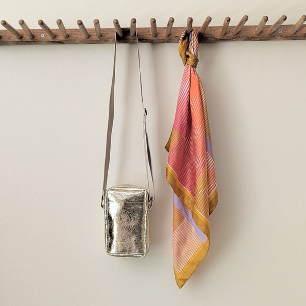 Gold crossbody bag and colorful striped scarf hanging on a wooden rack against a beige wall.

Stitch and Tickle unisex messenger travel bag adjustable strap shoulder crossbody leatherwork handmade sowa shop Boston gift shop store