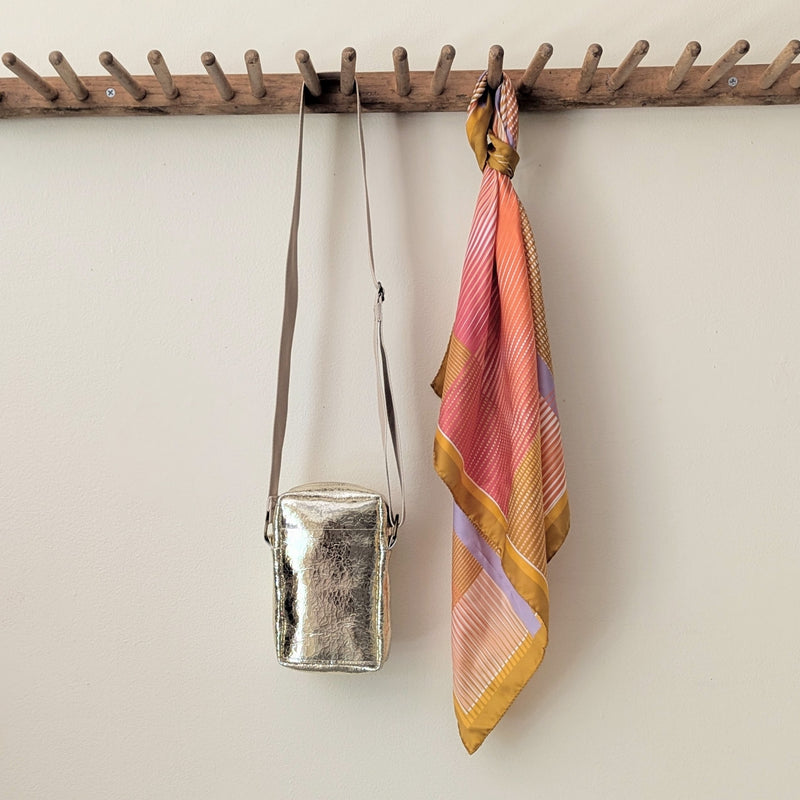 Gold crossbody bag and colorful striped scarf hanging on a wooden rack against a beige wall.

Stitch and Tickle unisex messenger travel bag adjustable strap shoulder crossbody leatherwork handmade sowa shop Boston gift shop store