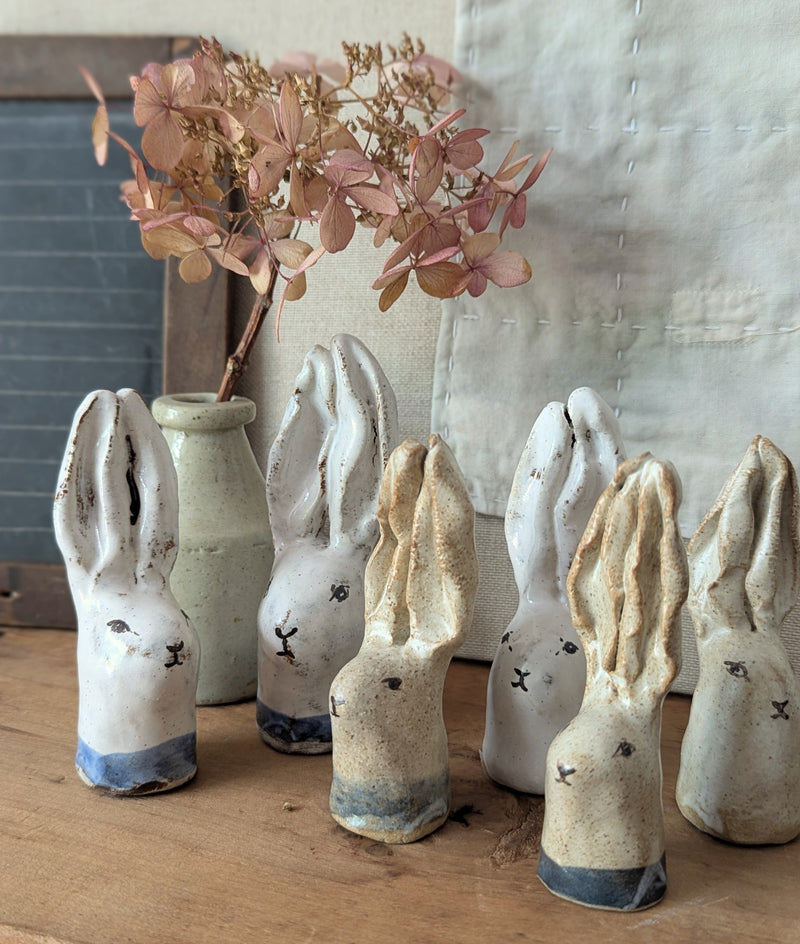 Set of ceramic rabbit figurines on a wooden surface with a vase and flowers in the background.

Handmade and hand-painted rabbit head sculptures figurines by Charlotte salt small business sowa Boston gift shop boutique store