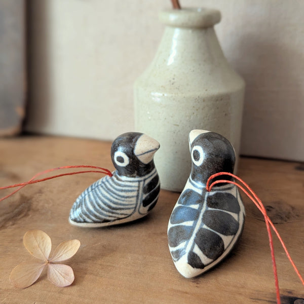 Two ceramic birds on strings with a vase in the background on a wooden surface.

Anna Hepler clar ceramic bird ornaments holiday figurines handmade hand painted New England Boston Massachusetts sowa gift shop store boutique