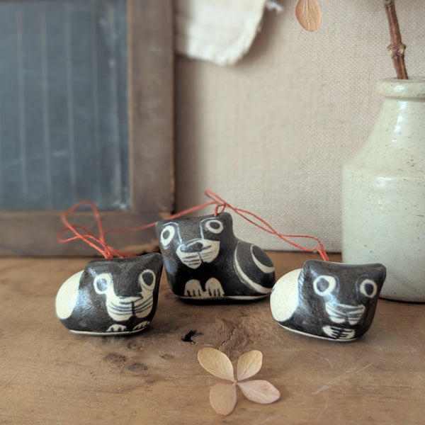 Three small ceramic cat-shaped ornaments on a wooden surface with a vase and chalkboard in the background.