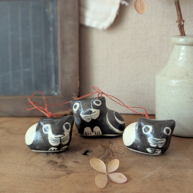 Three small ceramic cat-shaped ornaments on a wooden surface with a vase and chalkboard in the background.