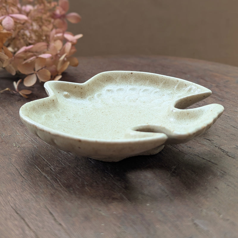 Ceramic bird-shaped dish on a wooden surface with dried flowers in the background