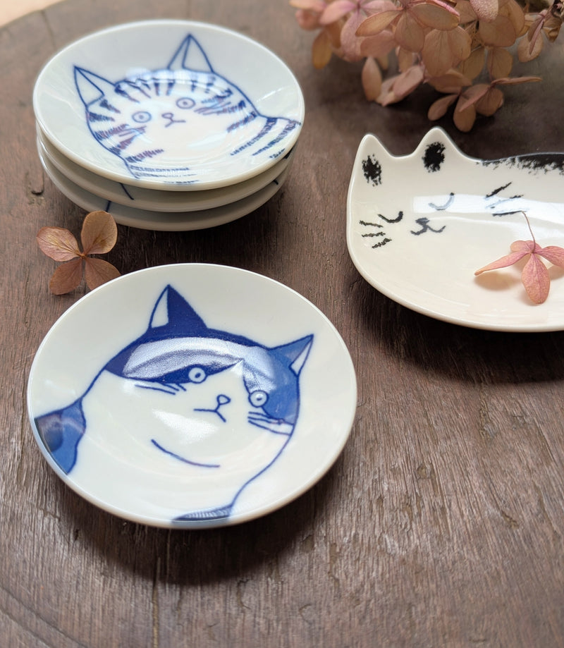 Set of small ceramic dishes with cat designs on a wooden surface.