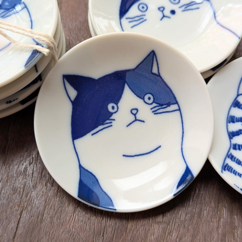 Set of small white plates with blue cat illustrations on a wooden surface
