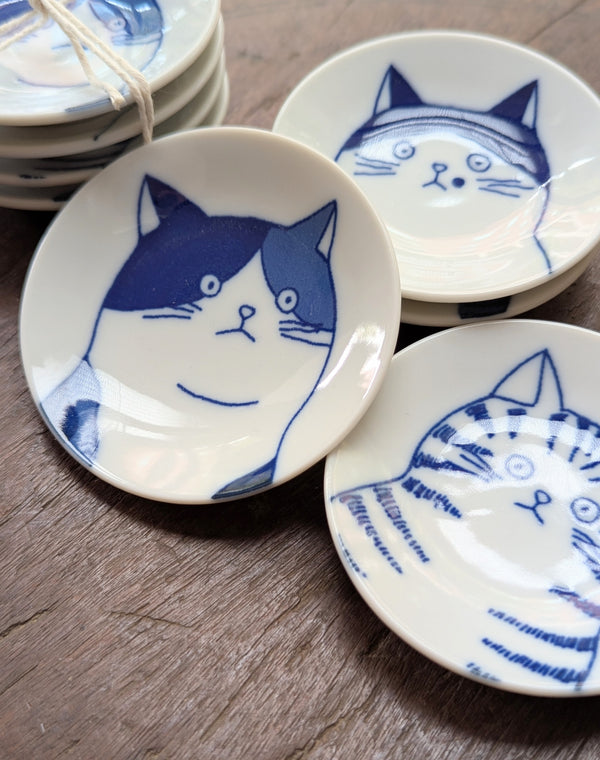 Set of small white plates with blue cat illustrations on a wooden surface