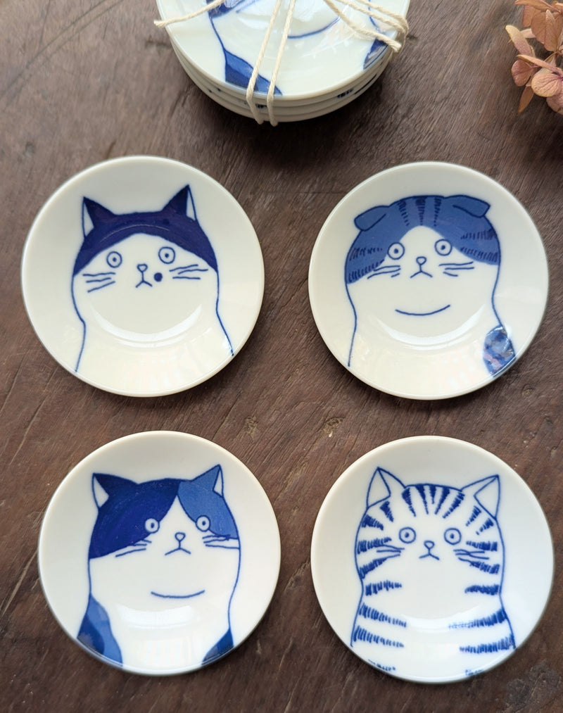 Four small ceramic plates with blue cat illustrations on a wooden surface.