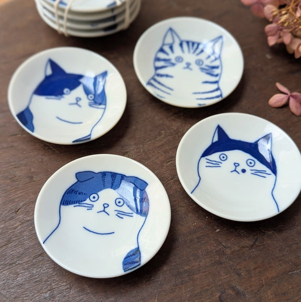 Four small white plates with blue cat illustrations on a wooden surface.