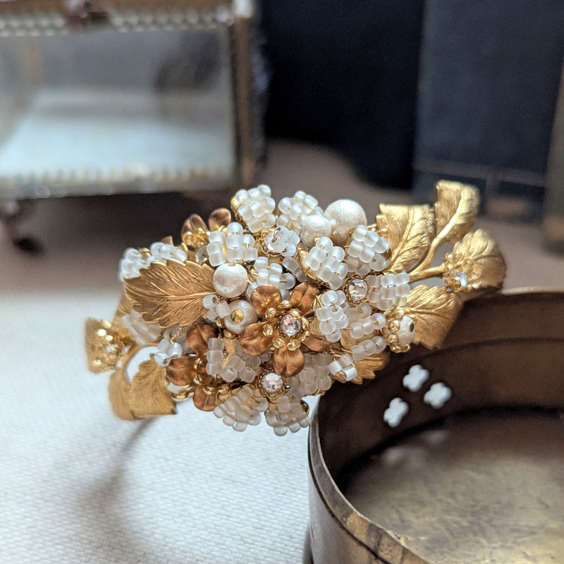 Large leaf shaped brass cuff bracelet with beaded, pearl, and crystal accent on a textured surface