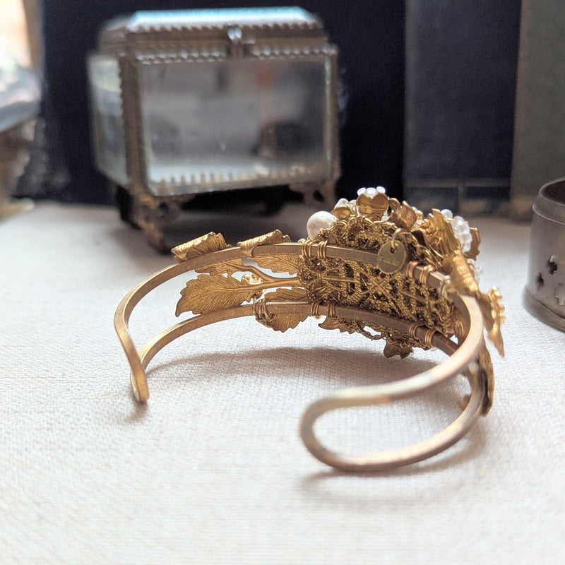 Large leaf shaped brass cuff bracelet with beaded, pearl, and crystal accent on a textured surface