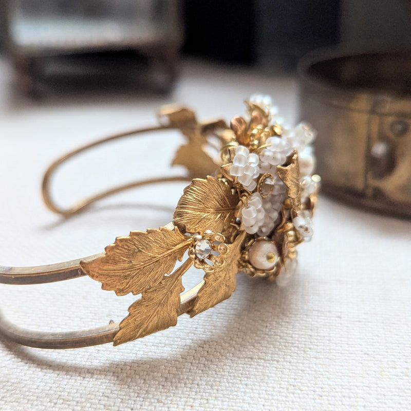 Large leaf shaped brass cuff bracelet with beaded, pearl, and crystal accent on a textured surface