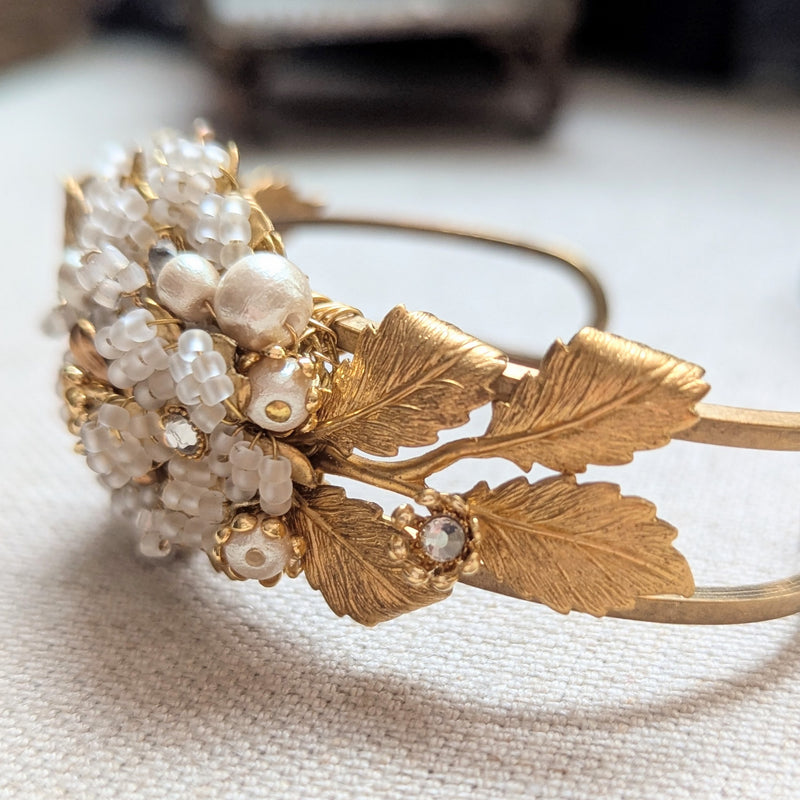 Large leaf shaped brass cuff bracelet with beaded, pearl, and crystal accent on a textured surface